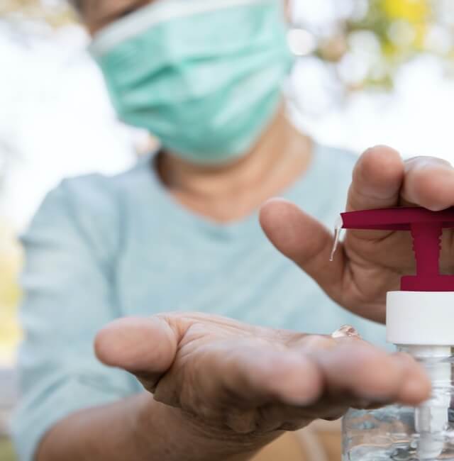 Person with surgical mask pouring sanitizing gel into their onw hands